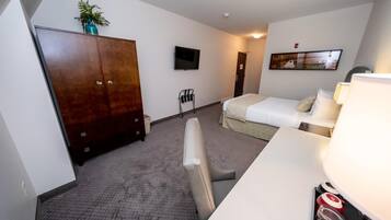 Een hotelkamer met een bed, een bureau, een kledingkast, een televisie en een schilderij aan de muur.