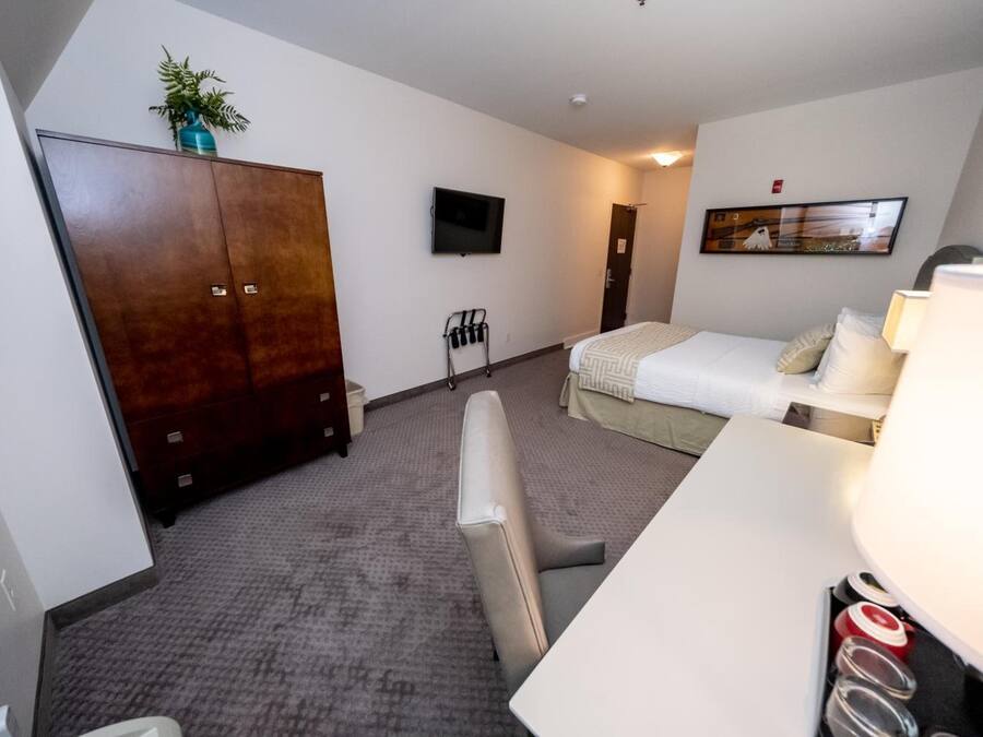 Een hotelkamer met een bed, een bureau, een kledingkast, een televisie en een schilderij aan de muur.