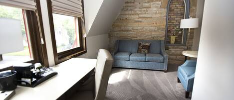 A cozy room with a desk, a blue sofa, and a stone wall.
