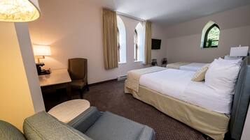 A hotel room with a bed, a desk, a chair, and two windows with curtains.