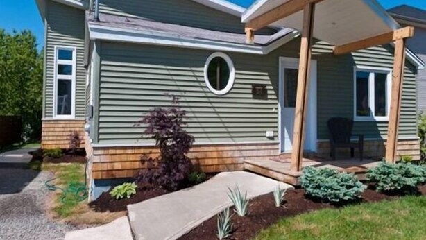 Una casa a un piano con veranda coperta, un'entrata e un piccolo giardino con diverse piante.