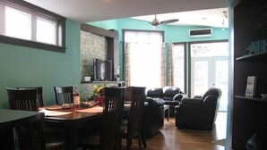 Zona pranzo con tavolo e sedie in legno, parete decorativa in pietra e televisore.
