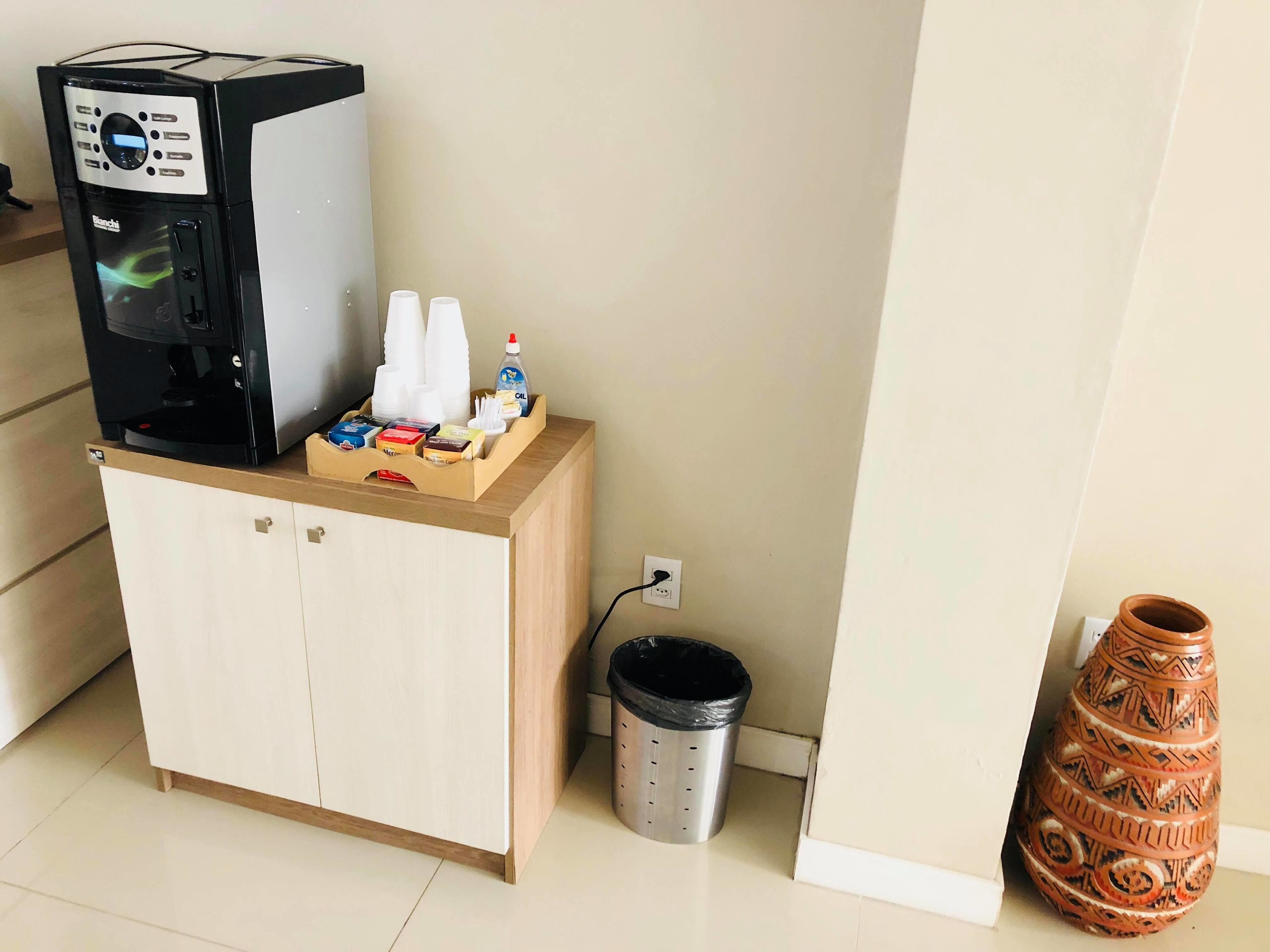 Une petite cuisine équipée d’une machine à café, de tasses, d’un flacon de liquide vaisselle et d’une poubelle.