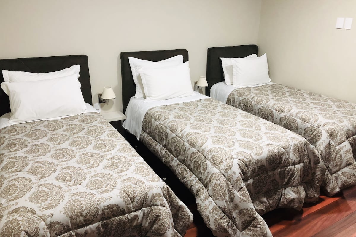 Ein Hotelzimmer mit drei Einzelbetten, jedes mit einer gemusterten Tagesdecke und weißen Kissen.