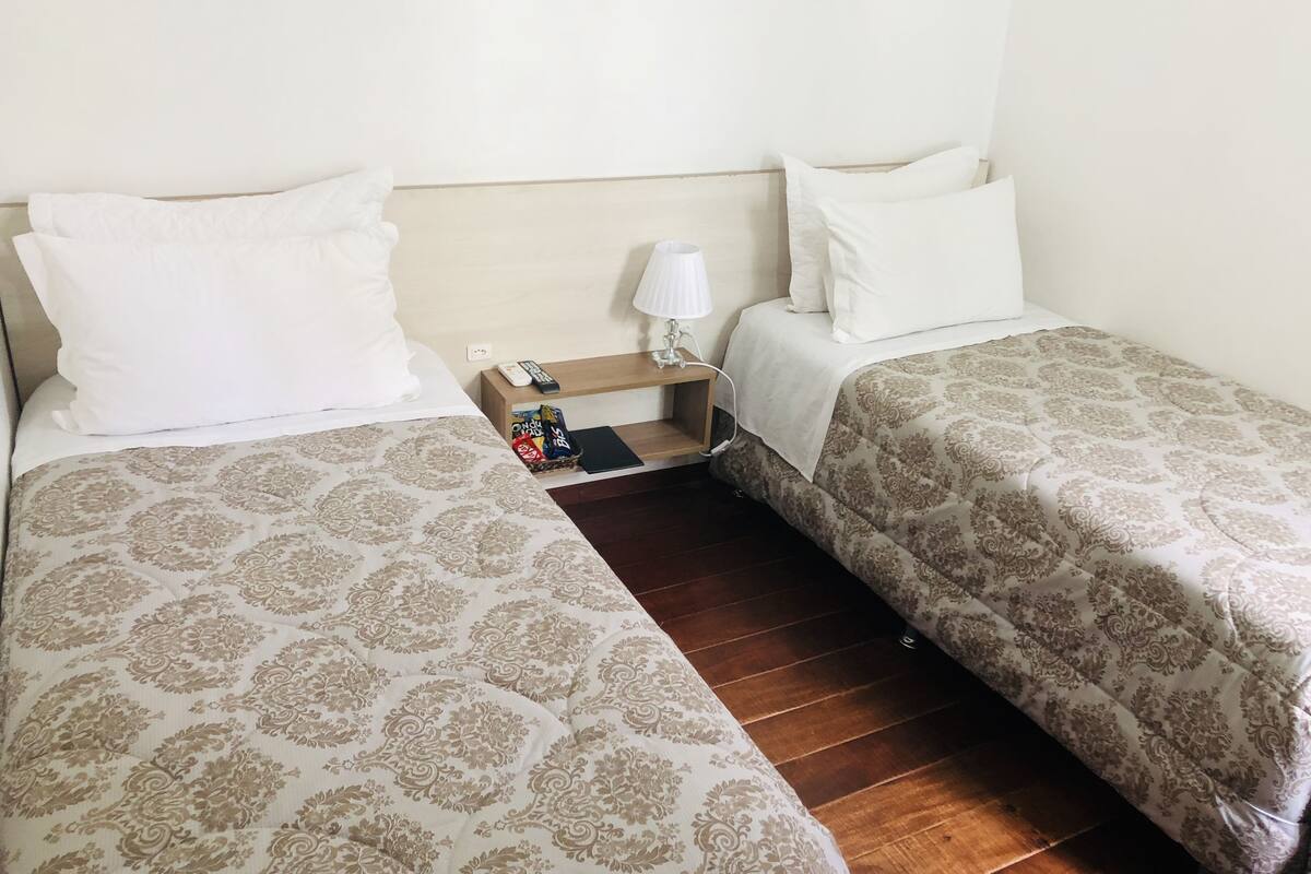 Ein Doppelzimmer mit Holzboden, einem Nachttisch mit Lampe und einem kleinen Tisch mit Snacks.