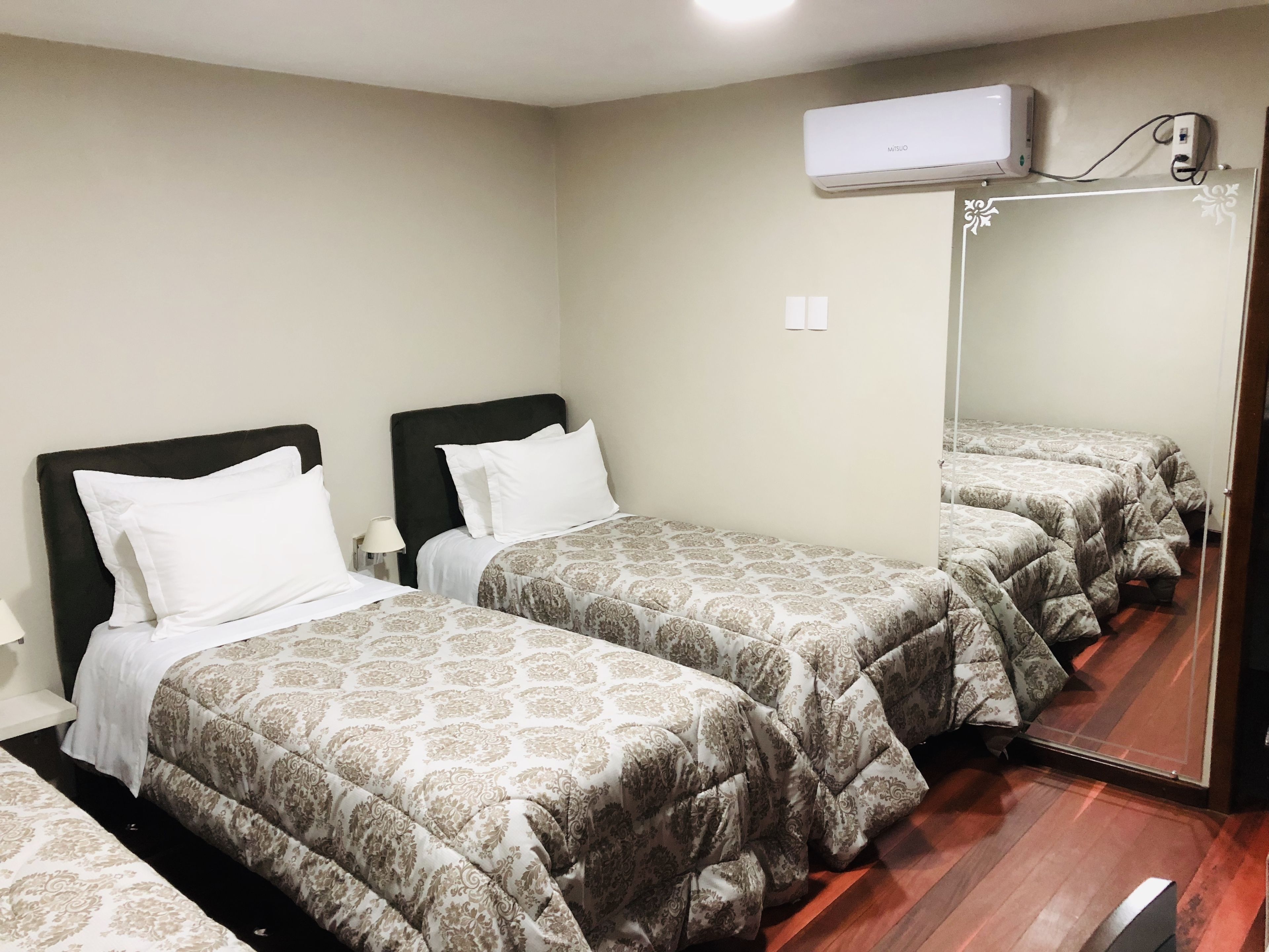 Una habitación de hotel con dos camas, un espejo grande y un equipo de aire acondicionado.