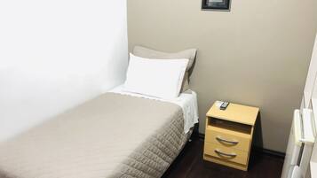 A single bed with a beige quilt, a white pillow, and a wooden nightstand with drawers.
