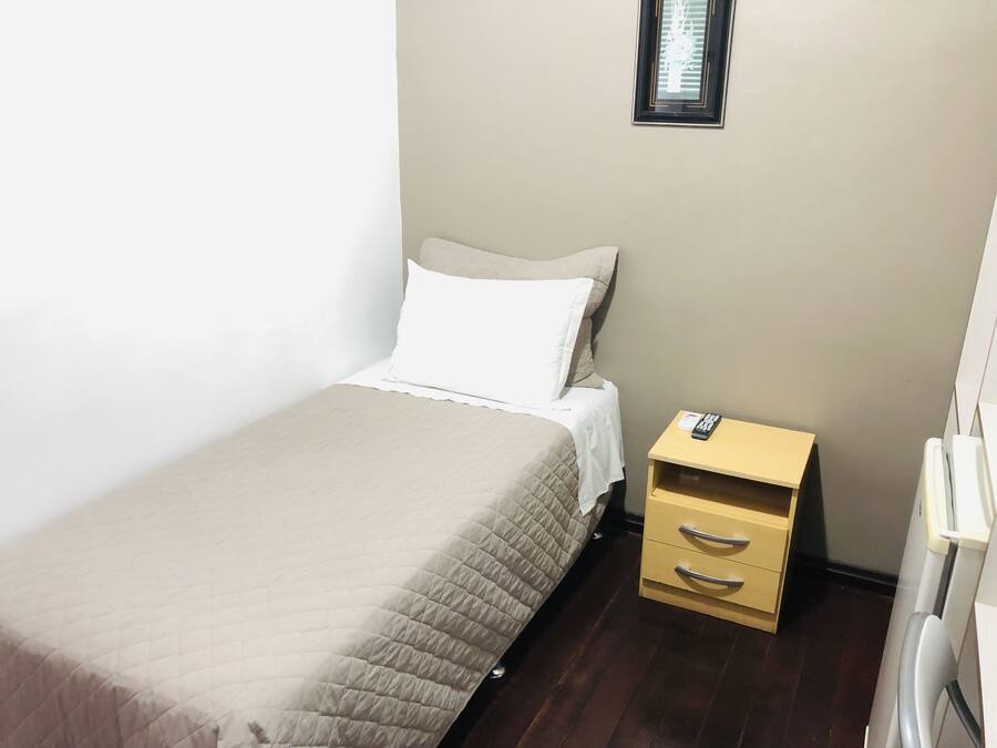 A single bed with a beige quilt, a white pillow, and a wooden nightstand with drawers.