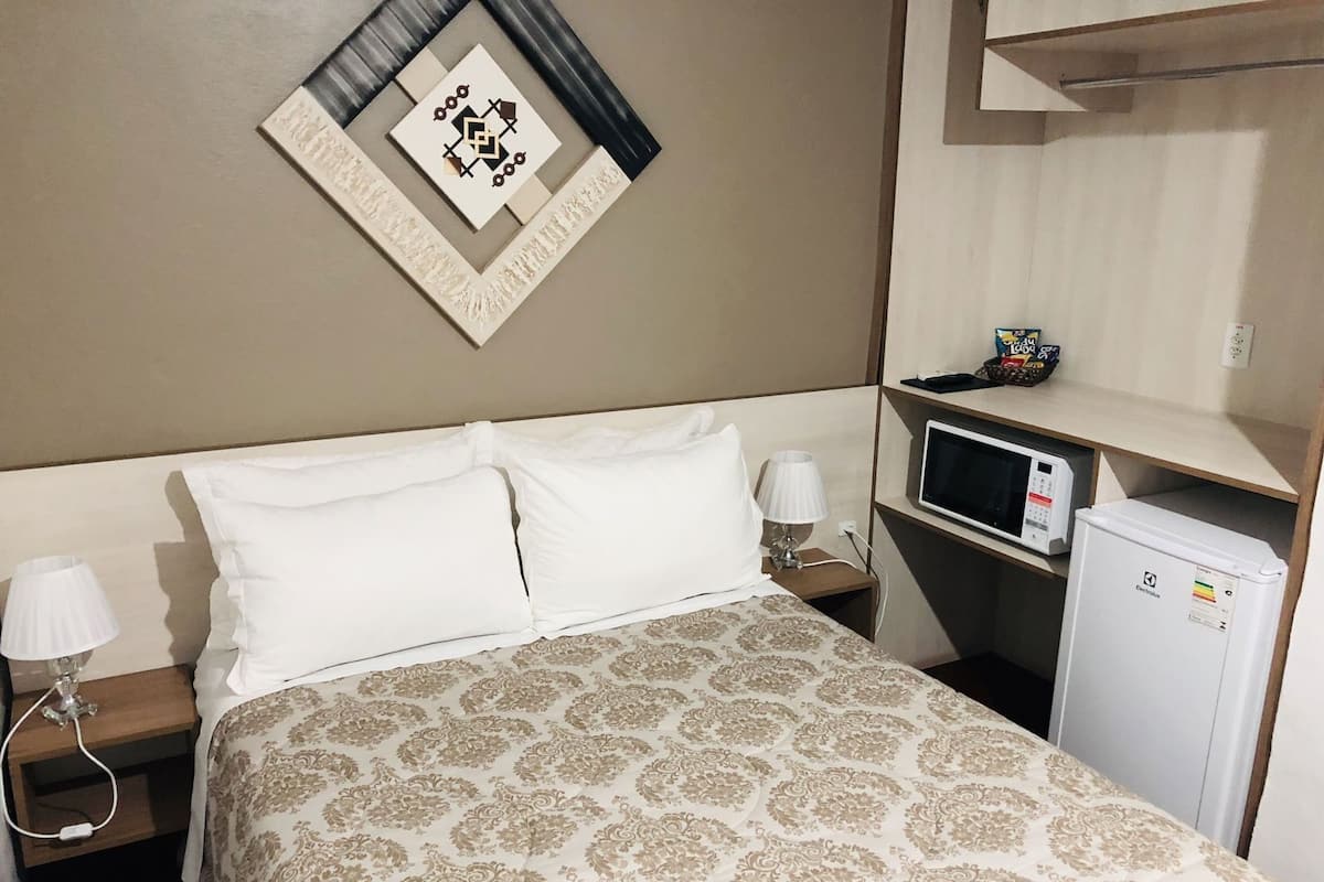 Ein Hotelzimmer mit Bett, zwei Nachttischlampen, einer Mikrowelle und einem Kühlschrank.