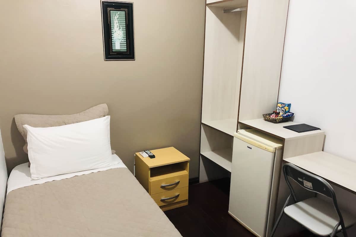 Ein Hotelzimmer mit Bett, kleinem Schreibtisch mit Stuhl, Schrank und einem gerahmten Bild an der Wand.
