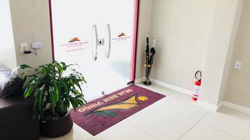A hotel reception area with a reception desk, a potted plant, a fire extinguisher, and a doormat with the hotel's name.