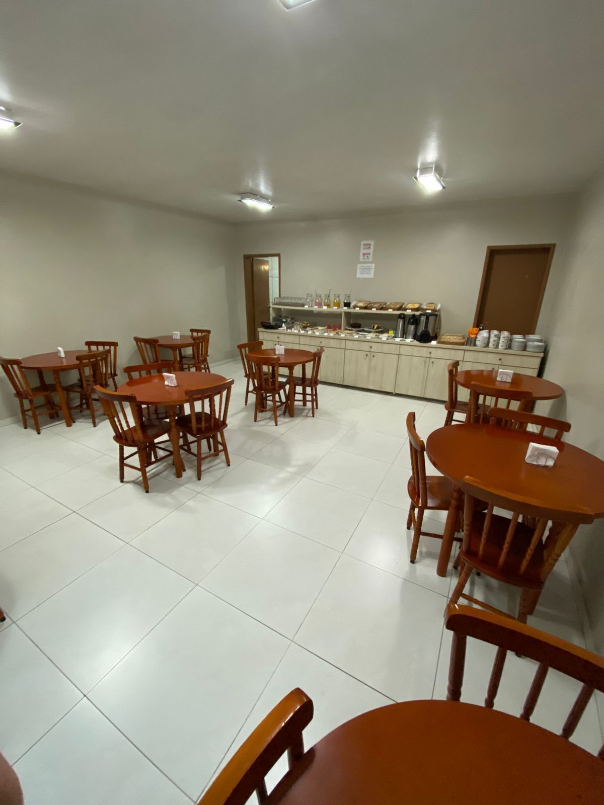 A dining area with wooden tables and chairs, a kitchen area with various appliances and food items, and a tiled floor.