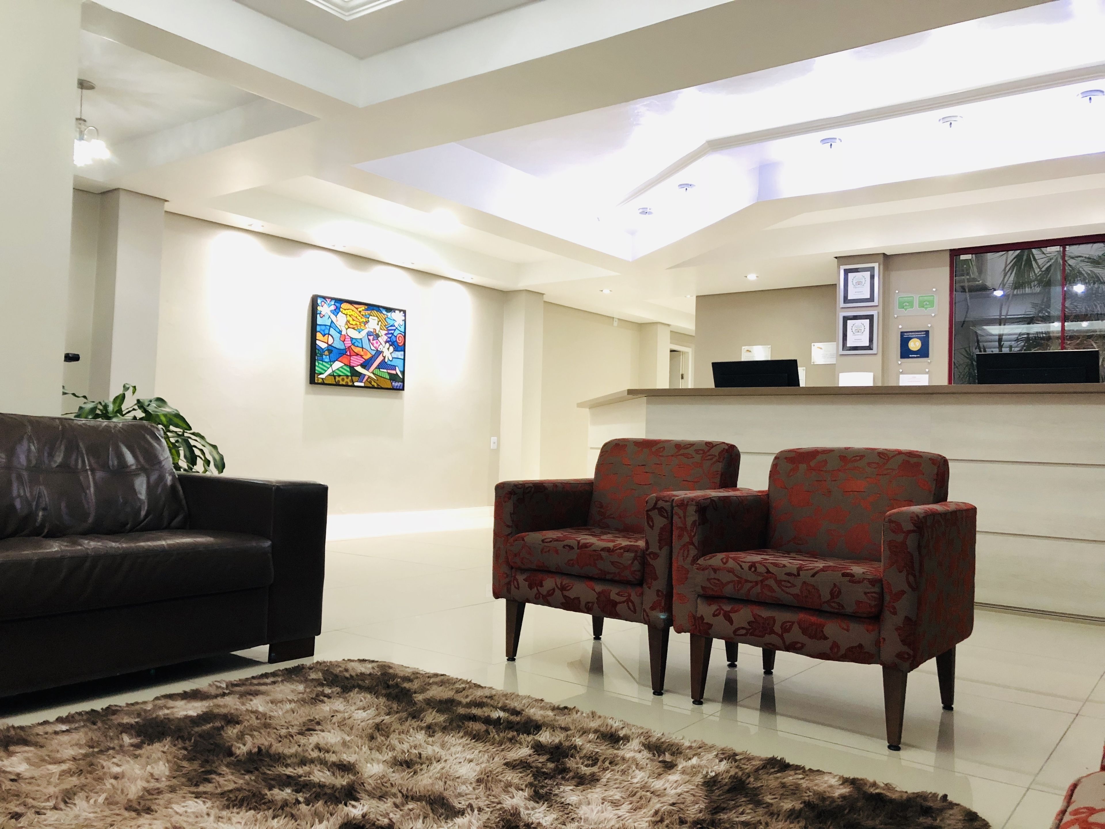 A modern living room with a black leather sofa, two patterned armchairs, a shaggy rug, and a ceiling with skylights.