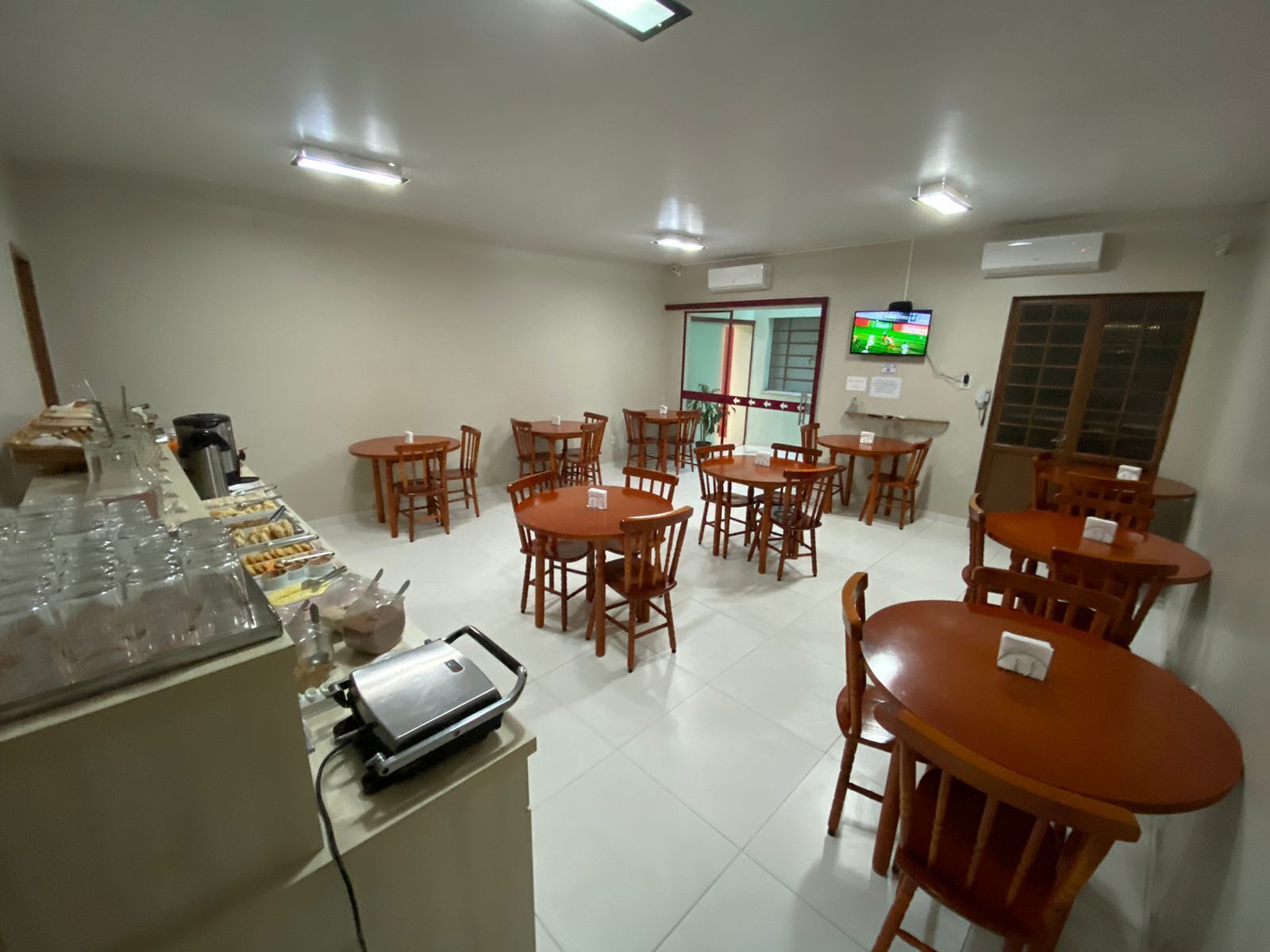 A dining area with multiple tables and chairs, a buffet with food items, and a television screen on the wall.