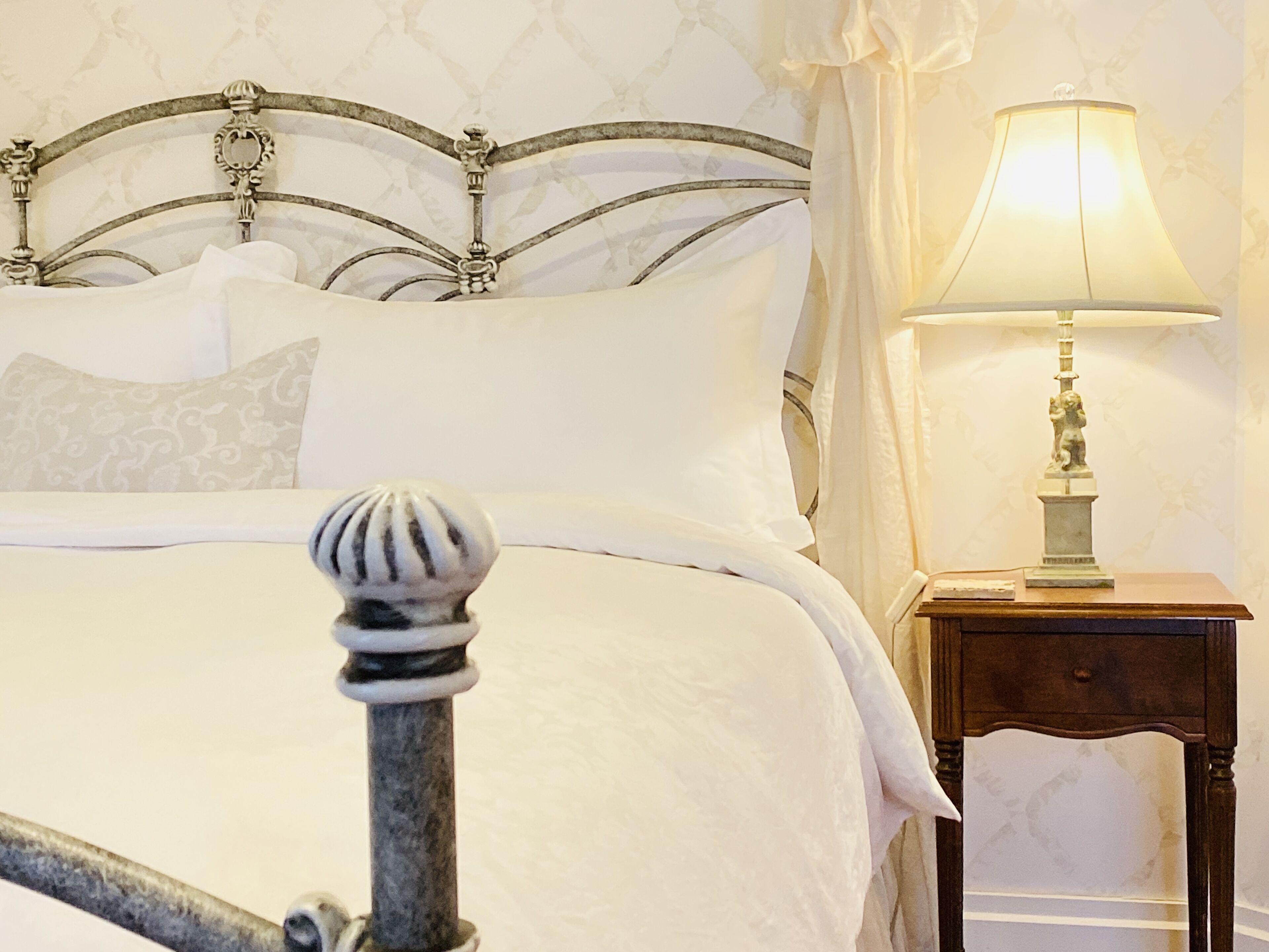 A bed with a metal headboard, white bedding, and a bedside table with a lamp.