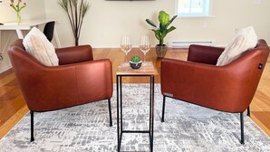 A living room with two brown leather chairs, a small table with two wine glasses, a potted plant, and a TV on the wall. - Princess and the Pea Hotel (Langley)