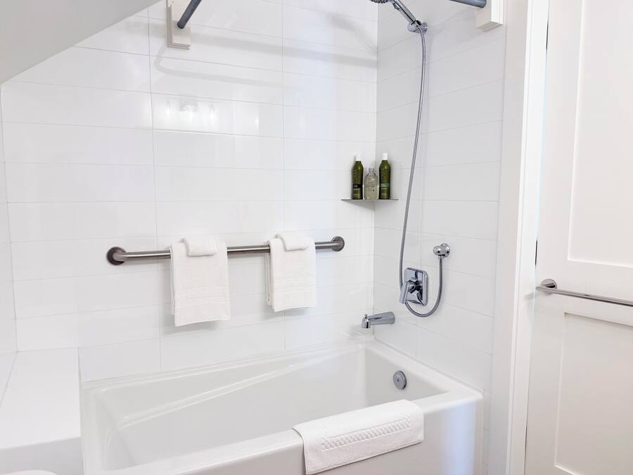 Uma casa de banho moderna com banheira, chuveiro e um porta-toalhas com três toalhas.