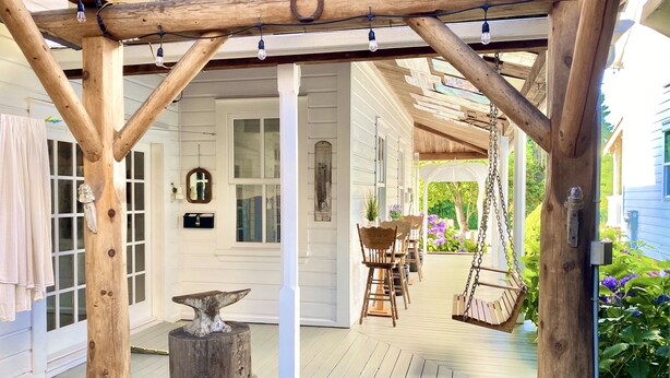 A wooden porch with a swing, a rustic anvil, and a cart. - Princess and the Pea Hotel (Langley)