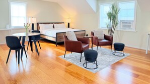 A modern bedroom with a bed, a dining table, two chairs, a small side table, a potted plant, and a large window. - Princess and the Pea Hotel (Langley)