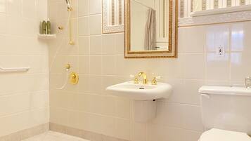 Un baño con lavamanos blanco, detalles dorados, inodoro y ducha con cabezal de ducha dorado.