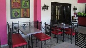 A dining area with booths and tables, a painting of fruits on the wall, and a black door. - Hotel San Francisco (Culiacan)