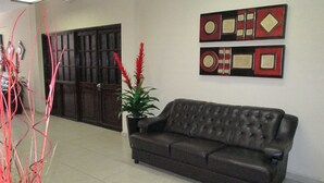 A room with a dark brown leather sofa, a potted plant with red foliage, and two framed abstract artworks on the wall. - Hotel San Francisco (Culiacan)