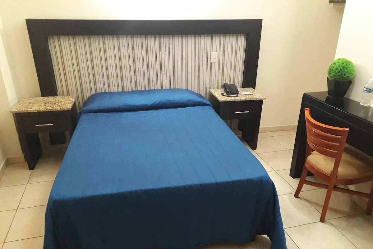 A hotel room with a bed, a desk, a chair, and a small potted plant.