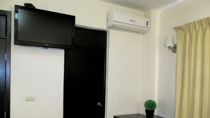 A room with a black door, a small table with a chair, a potted plant, and a mounted air conditioner. - Hotel San Francisco (Culiacan)