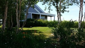 A modern house with a sloped roof, surrounded by lush greenery and flowering plants. - Beach House Comfort (Cocagne)