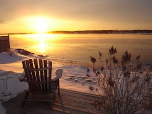 A wooden deck with a chair facing a frozen lake at sunset. - Beach House Comfort (Cocagne)