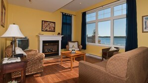 Ein Wohnzimmer mit Kamin, einer Couch, einem Sessel, einem Tisch und Meerblick durch ein großes Fenster.