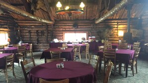 Un interior rústico de madera con mesas redondas cubiertas con manteles morados y sillas de madera.
