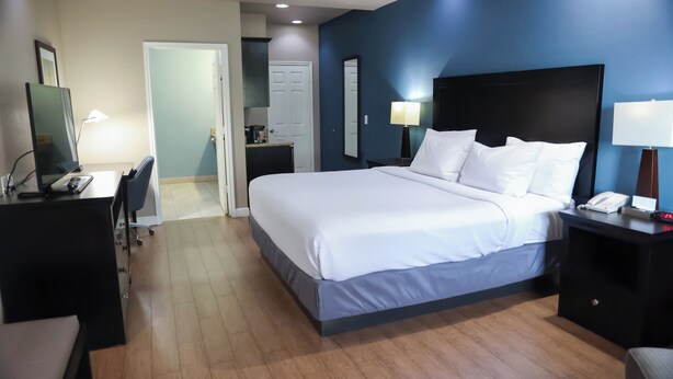 A hotel room with a bed, desk, chair, and bedside lamps. - Black Gold Inn (Yoakum)