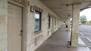 A covered corridor with stone walls and doors, leading to a parking lot. - Black Gold Inn (Yoakum)