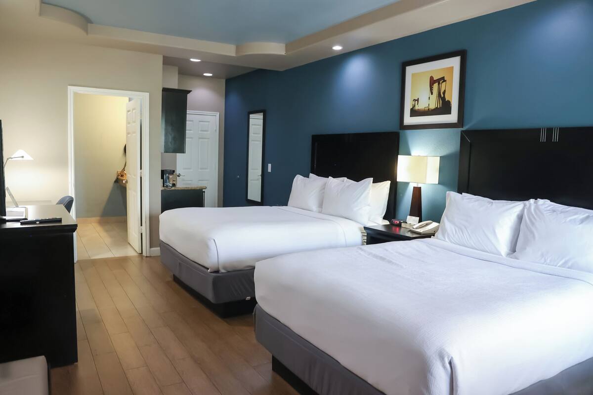 Quarto de hotel com duas camas, uma escrivaninha, uma cadeira, mesa de cabeceira, abajur, espelho e um quadro na parede.