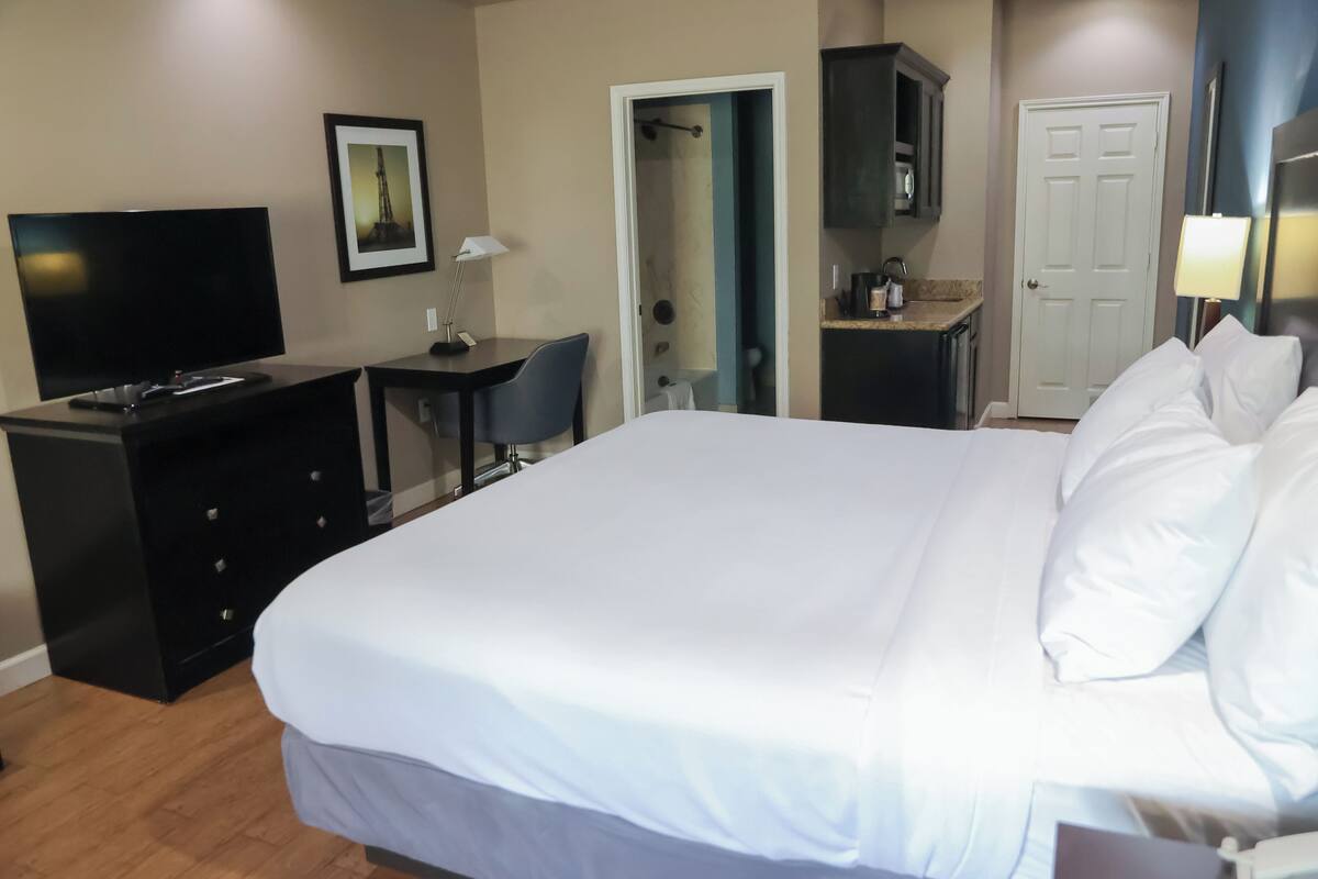 Quarto de hotel com uma cama grande, televisão, escrivaninha e porta para o banheiro.