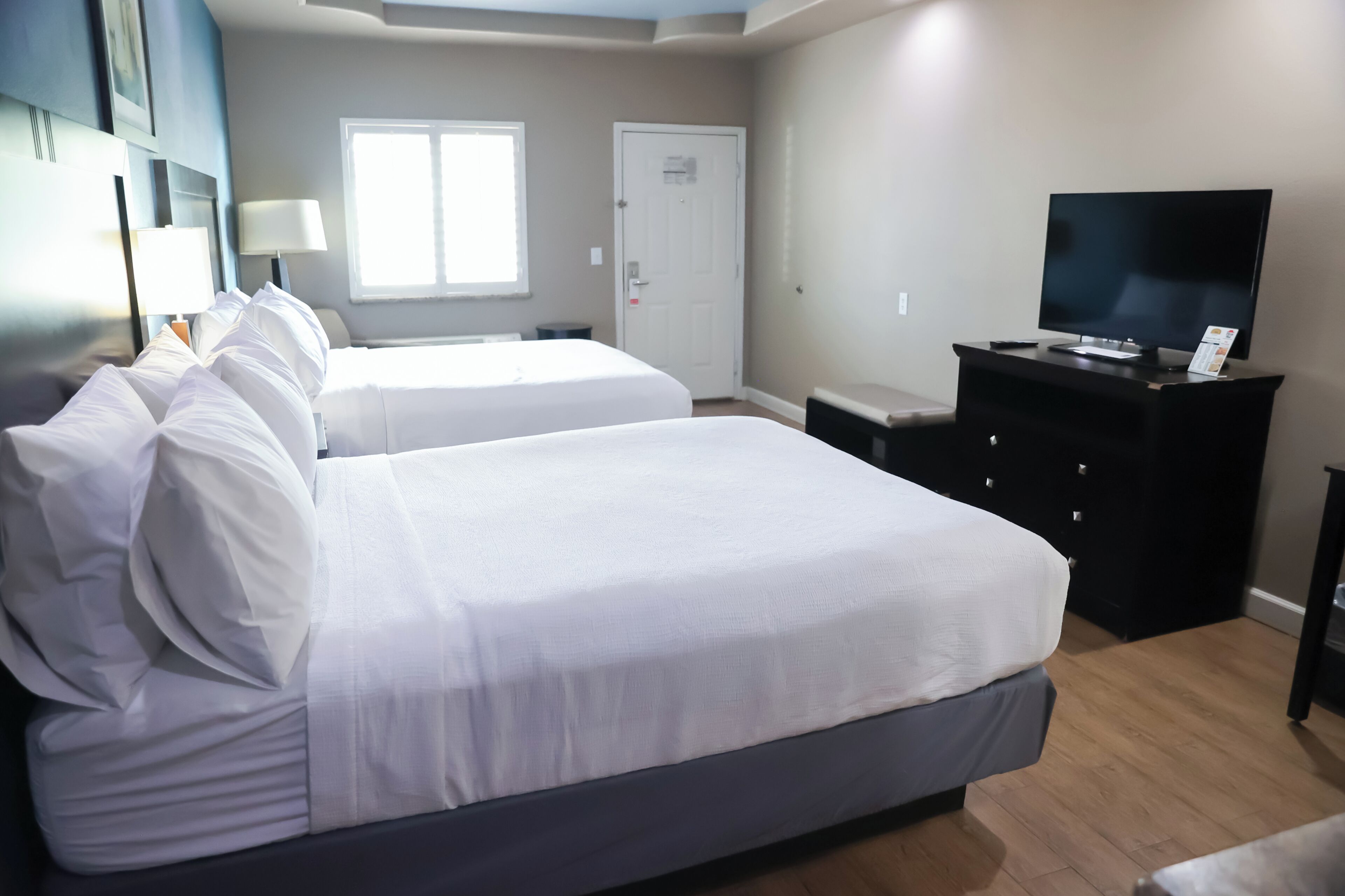 A hotel room with two beds, a TV, a dresser, and a window.