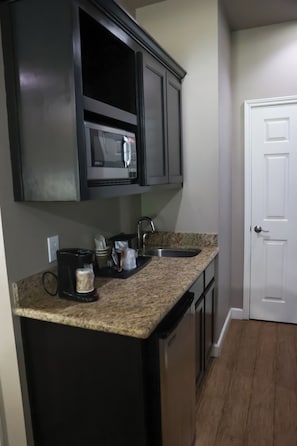 A kitchen with dark cabinets, a microwave, a coffee maker, and a sink.