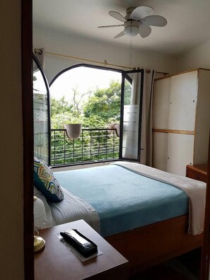 A bedroom with a bed, a bedside table, a wardrobe, and a balcony with a view of greenery. - Casa Echavarria (San Pedro)