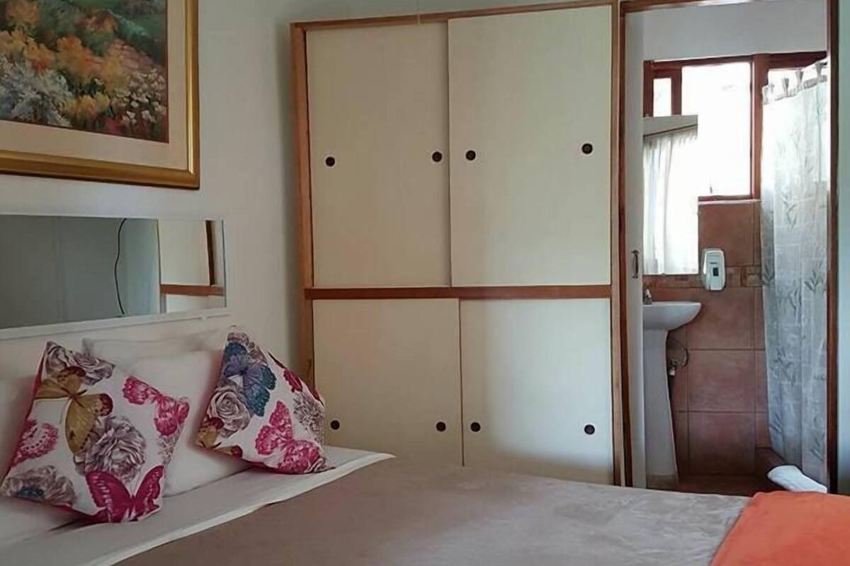 A bedroom with a bed, a wardrobe, a painting, and a bathroom visible through an open door.