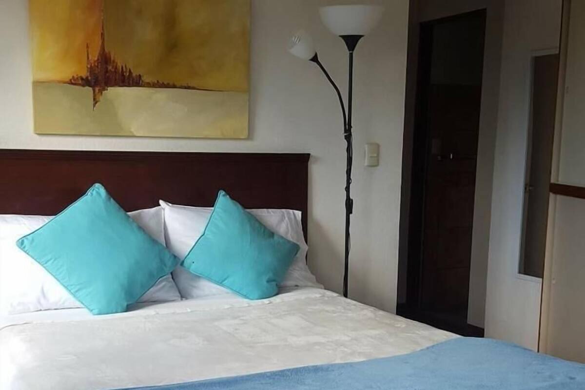 A neatly made bed with a white and blue bedspread, two turquoise pillows, and a dark wooden headboard.