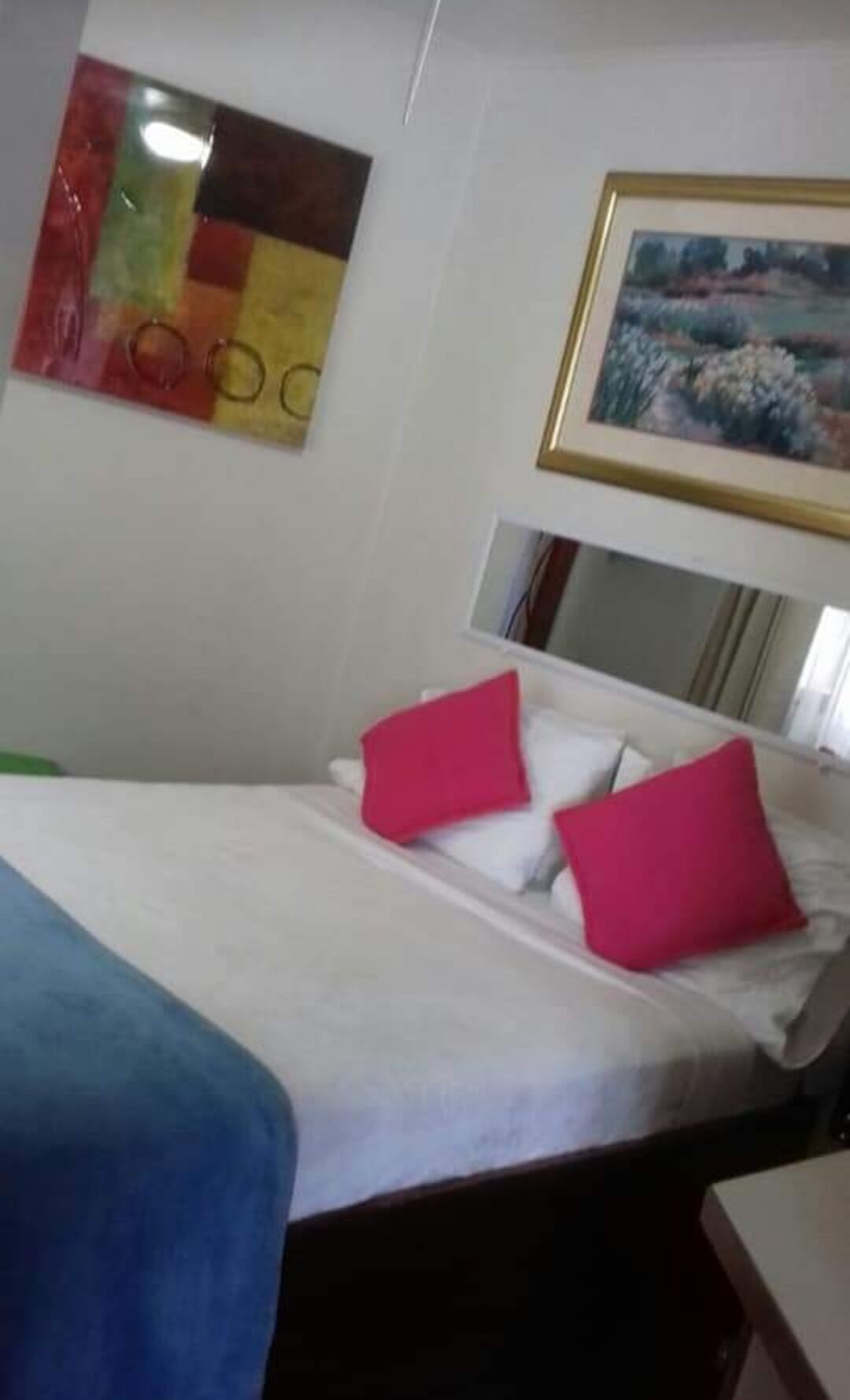 A hotel room with a bed, white bedding, and two red pillows.