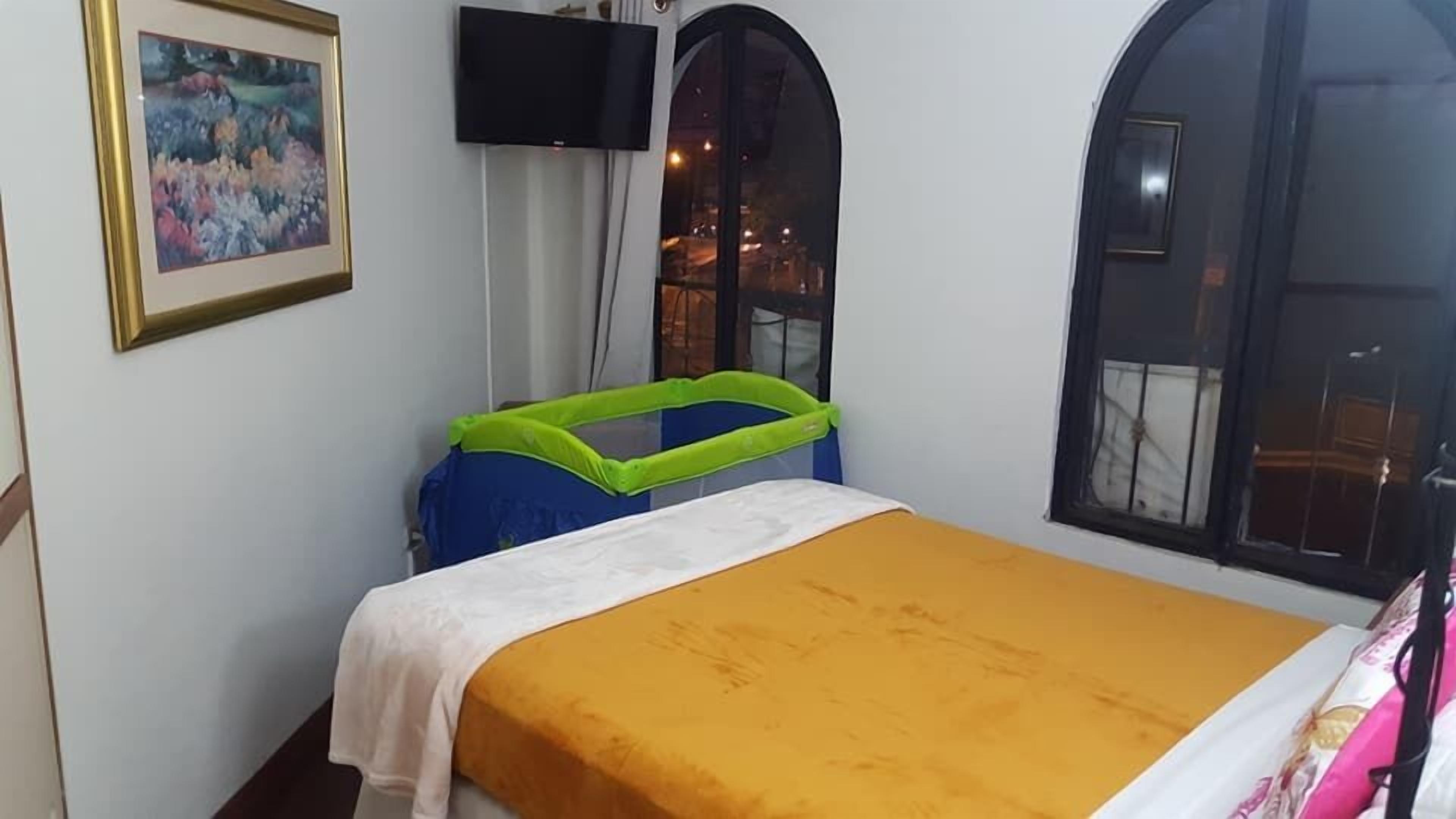 Une chambre avec un lit, un téléviseur fixé au mur et une fenêtre à arc.