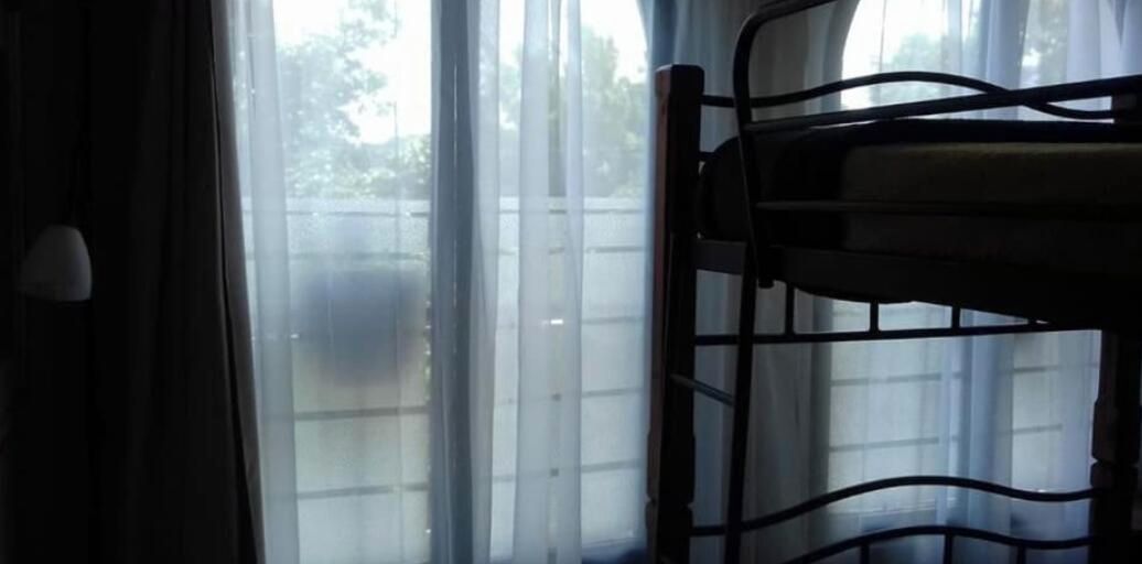 A window with a view of a fence and trees, a metal chair, and a lamp.