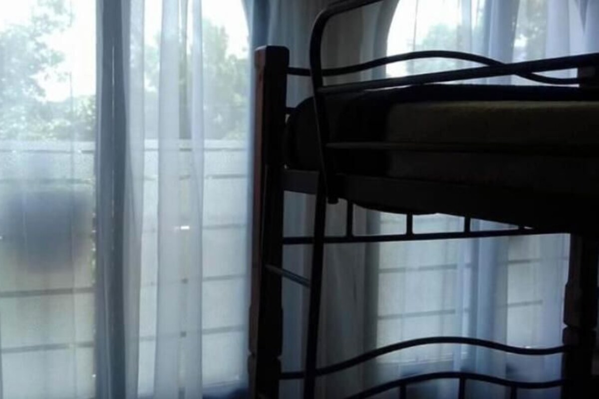 A window with a view of a fence and trees, a metal chair, and a lamp.