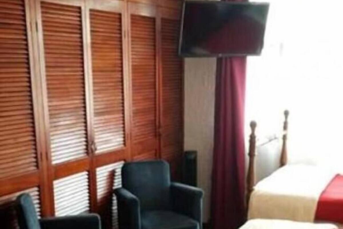 A hotel room with two beds, a television, a chair, and a window with blinds.