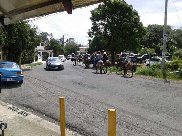 A street scene with a blue car parked on the side, a group of people on horseback, and a building with a covered entrance.