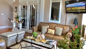 A living room with a brown leather sofa, a glass coffee table, and a TV mounted on the wall.
