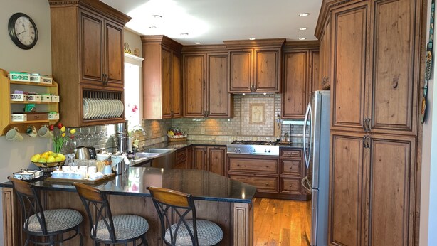 A modern kitchen with wooden cabinets, a central island with bar stools, stainless steel appliances, and a decorative backsplash.