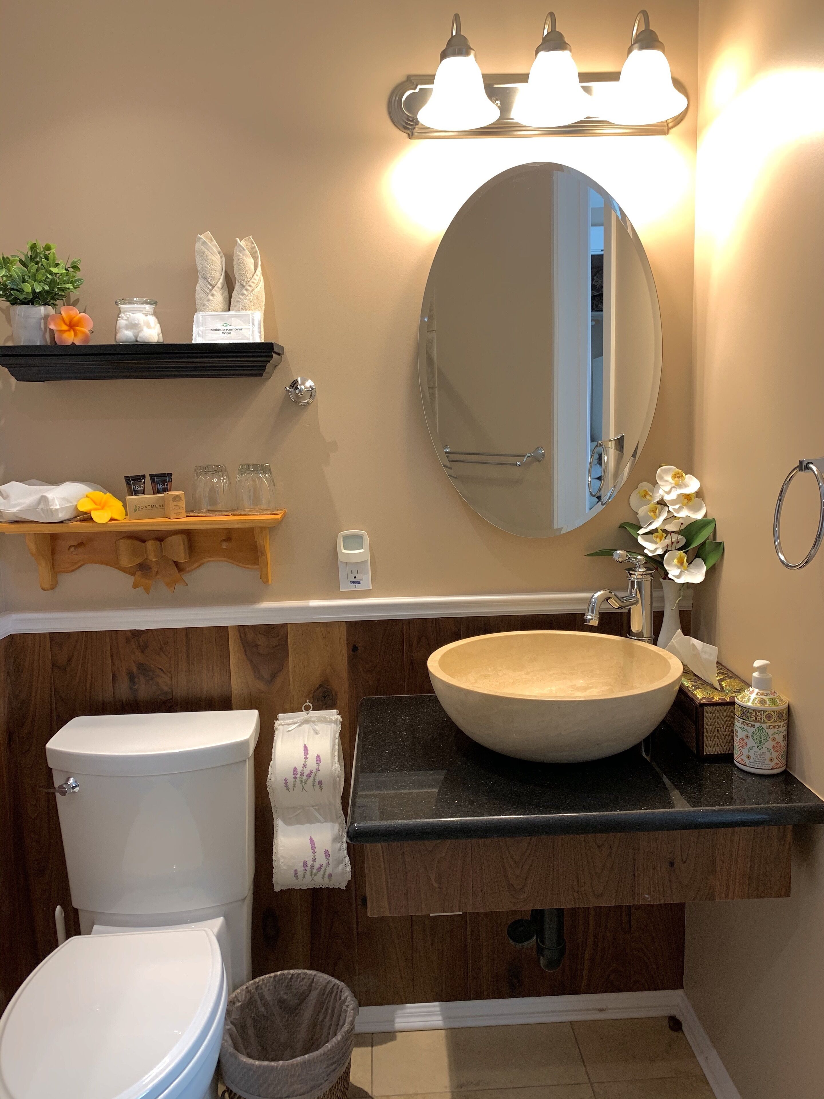 Un baño con tocador de madera, un lavamanos ovalado grande, un inodoro y un espejo con luces arriba.